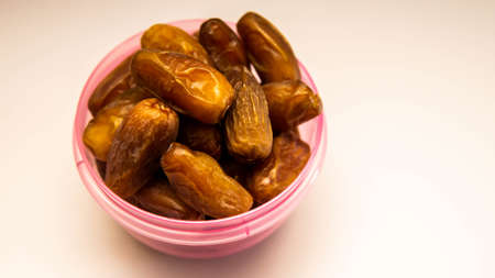 Phoenix dactylifera, commonly known as dates or kurma in purple plastic container on isolated white...