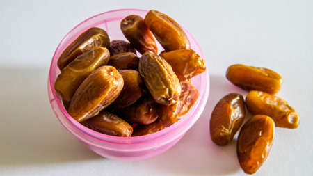 Phoenix dactylifera, commonly known as dates or kurma in purple plastic container on isolated white...