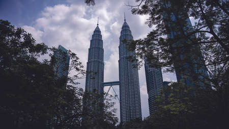 Kuala Lumpur, Malaysia - July 30, 2019: Low angle view of the famous Petronas Twin Tower or KLCC from the green tree nature with cold color backgrounds.のeditorial素材