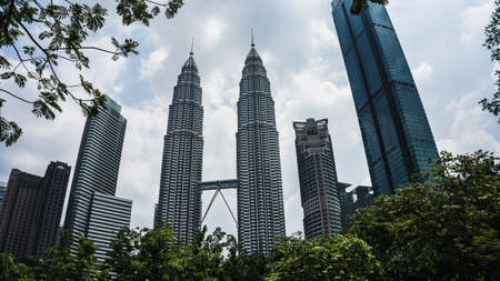 Kuala Lumpur, Malaysia - July 30, 2019: The low angle view of the Petronas Twin Towers or KLCC in the city surrounding with tall skyscrapers and clear cloudy blue sky during the day.のeditorial素材