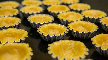 Close up view of making process egg tart in a mold on a black tray. It is a kind of custard tart of...