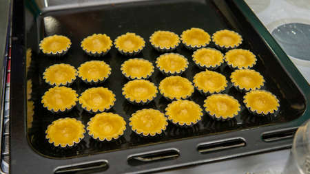 Close up view of making process egg tart in a mold on a black tray. It is a kind of custard tart of...
