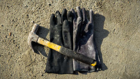 Flat lay of rusty metal hammer and construction white hand glove on grunge cement background with natural light and shadow. Labor day concept with empty copy space.の写真素材