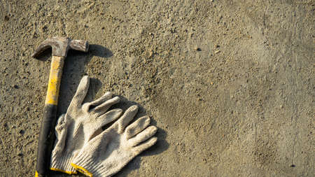 Flat lay of rusty metal hammer and construction white hand glove on grunge cement background with...