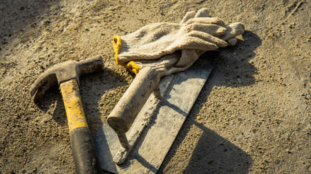 Flat lay of rusty metal hammer, finishing trowel and construction white hand glove on grunge cement background with natural light and shadow. Labor day concept with empty copy space.の写真素材