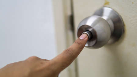 Close up view hand finger pressing the lock button of metal brass door knob to close the door. A...