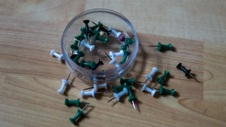 Top view of full thumb tacks in a transparent box and scattered on wooden background. It is a short nail or pin used to fasten items to a wall or board for display. Selective focus on foreground.の写真素材