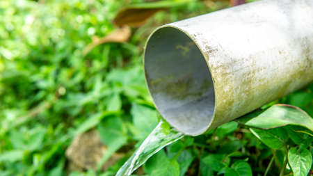 Close up view drain water flowing from the PVC pipe hole. Sanitary sewer concept. Transporting water from rain and houses for disposal. Rural environment sewage system. Selective focus on foreground.の写真素材