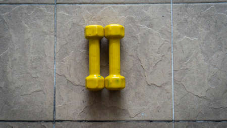 A pairs of 1 kilogram yellow mini dumbbells on the floor with natural light. Exercise tool and...
