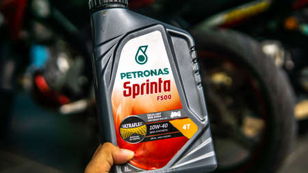 Bangi, Malaysia - July 24, 2019: Hand holding the Petronas Sprinta F500 oil bottle with motorbike on...
