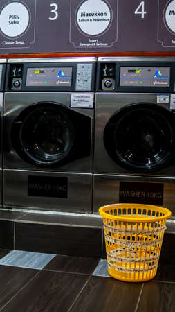 Bangi, Malaysia - July 28, 2019: A self service coin operated laundry machine at Mizz Launderette at Teras Jenang in Bangi. Selective focus. Laundry basket at the side of the washing machine.のeditorial素材
