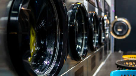 Side view of washing machine door in row. A self service coin operated laundry machine. Selective focus. Laundry basket at the side of the washing machine.の写真素材