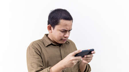 Serious and focus face expression of young Asian Malay man looking at the smartphone on isolated...