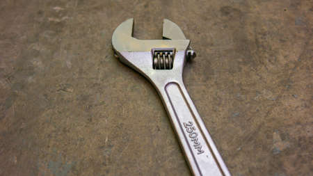 A metal adjustable wrench or spanner on isolated floor background. It is a tool used to provide grip...