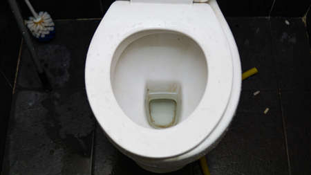 Top view of white toilet bowl with wet floor and cigarette on the floor. Selective focus on foregrounds.の写真素材