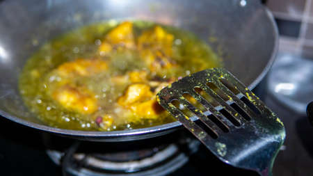 Close up view of a metal spatula with raw chicken meat fried in a wok with hot boiling oil at the kitchen as background. Homemade dish. Oil bubbles on surface of hot oil.の写真素材