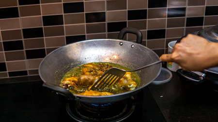 Close up view of a raw chicken meat fried in a wok with hot boiling oil at the kitchen. Hand preparing fried chicken using the metal spatula. Homemade dish. Oil bubbles on surface of hot oil.の写真素材
