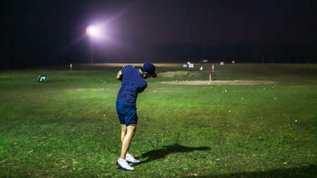 Selangor, Malaysia - September 17, 2019: A man with a short pants holding a golf club playing at the golf driving range on a green carpet mat during the night.のeditorial素材