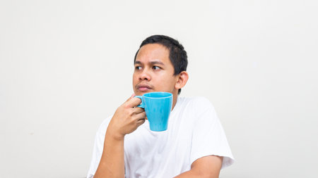 A portrait of Asian Malay man day dreaming and thinking on something with the blue tea cup on his hand.の写真素材