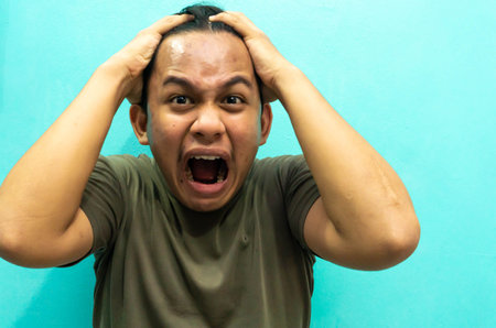 Portrait of young Asian man with headache on blue wall background.の写真素材