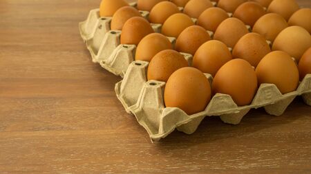 Brown chicken eggs in gray carton package box on brown wooden table
