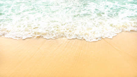 Golden brown sand on a beach with white foam on wave of pastel green color sea water, closeup imageの写真素材
