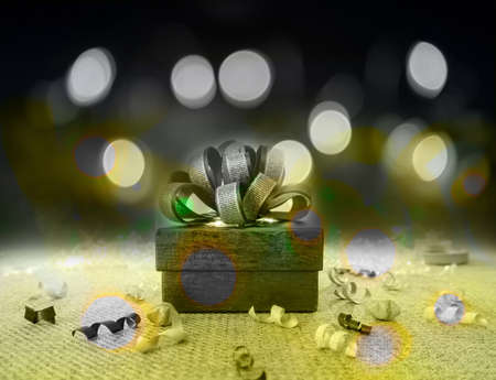 A grey gift box with gray ribbon on green fabric under bokeh yellow lighting on dark backgroundの写真素材