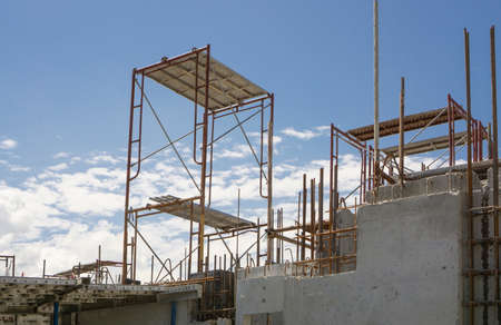 The steel scaffolding with brown rust standing on the top floor of the building under white fluffy clouds and blue skyの写真素材