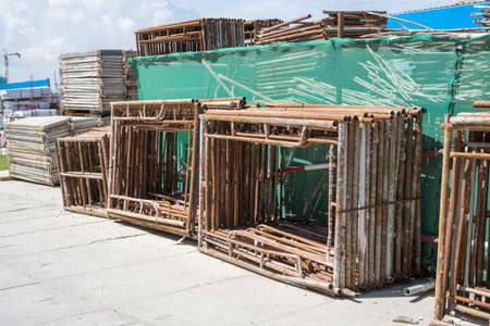 A pile of steel scaffolding with brown rust on the cocrete floor in front the building