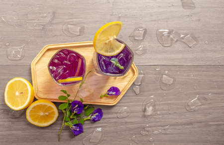 Two glasses of Blue and Violet Butterfly pea flower juice drinking, decorated with yellow lemon fruit sliced and fresh Asian pigeon wings flowers, on wooden table with ice, top view imageの写真素材