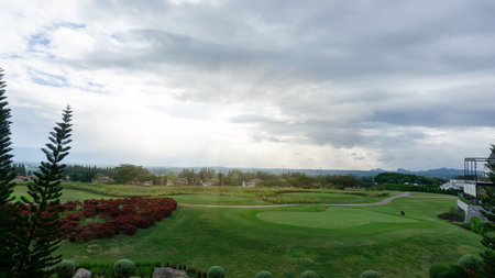 Landscape of green grass Lawn yard, golf course with a concrete walkway on lawn land, mountain in background under cloudy skyの写真素材