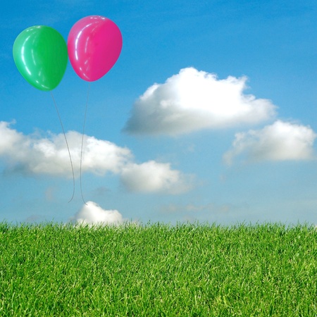 green-grass-with-floating-blue-and-pink-balloon-and-blue-skyの写真素材