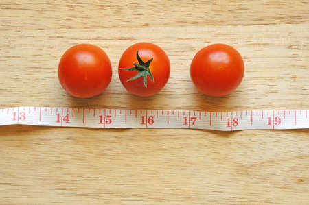 cherry tomatoes with measuring tape on wood background (diet concept)