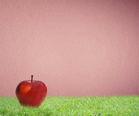 Red apple on green grass with pink wall as backgroundの写真素材