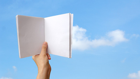 Hand holding blank white notebook over blue sky
