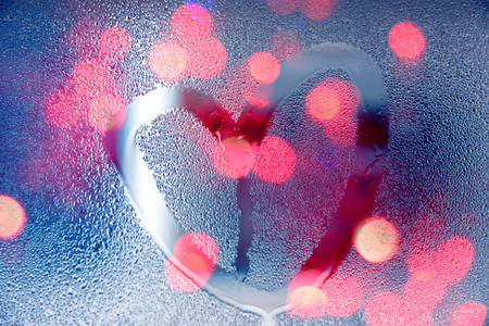 Rain at night, draw heart shape on wet glass with lightの写真素材