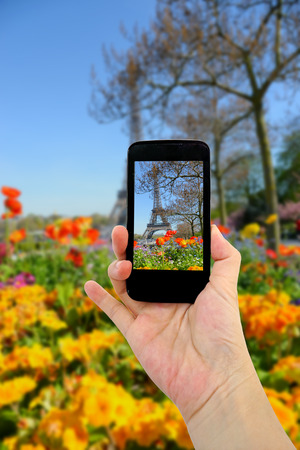 travel concept - tourist taking photo of Eiffel tower with colorful flowers in spring