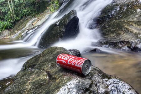 SELANGOR, MALAYSIA, OCTOBER 25, 2015 : Coca-cola cans on the rocks with waterfall background. Coca-Cola is the top selling soft drinks in the world.のeditorial素材