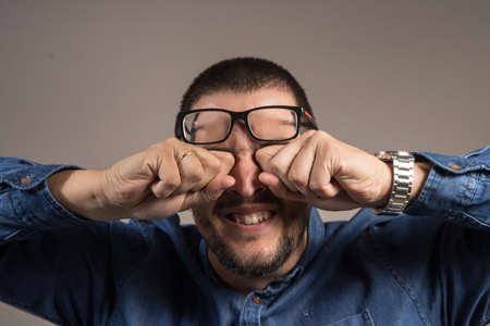 a gentleman with a beard scratching his eyes with glassesの写真素材