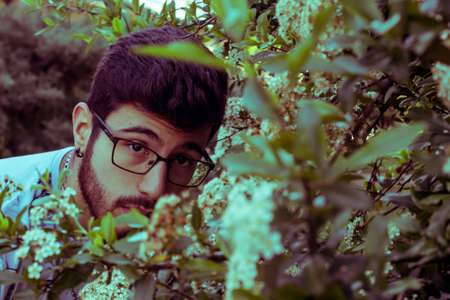 young man peeking through flowersの写真素材