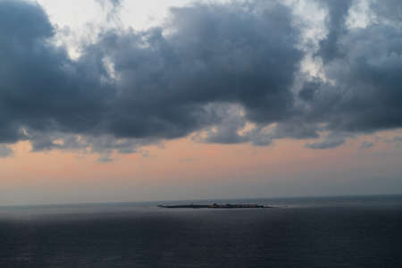 looking at island in the middle of the sea at sunrise with clouds in the skyの写真素材