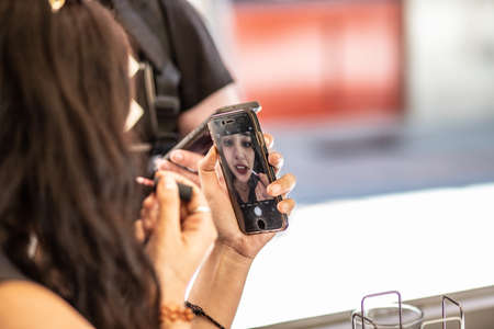 young woman, touching up makeup with smartphone camera