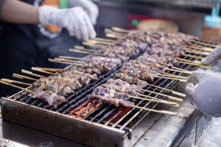 seller grilling tasty bbq meat with wooden skewers.の写真素材
