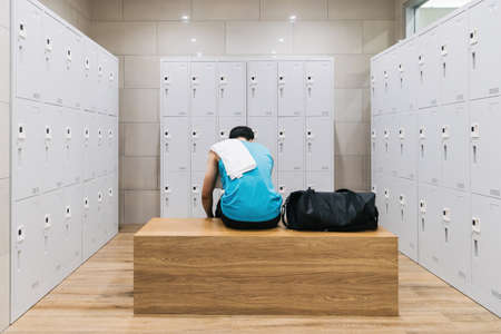 man with towel sitting on wooden bench in gym.の写真素材