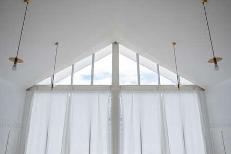 interior view of triangle shape glass window with white curtain and cloud sky.