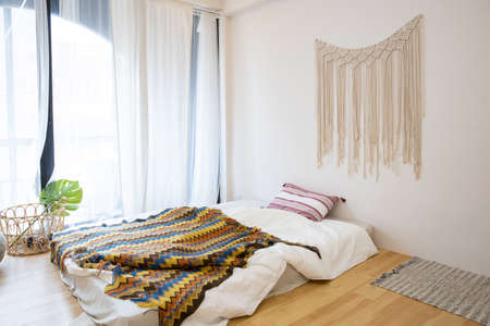 Interior view of white unmade messy bed on a wooden floor in the morning with transparent curtain...