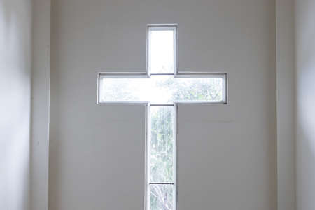 front view of interior transparent window cross shape with sunlight on white wallの写真素材