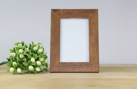 Photo frame mockup with white flowers on wooden table and gray wall backgroundの写真素材