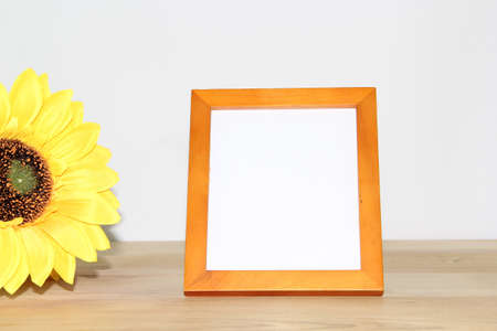 Blank photo frame with sunflower on wooden table against white wallの写真素材