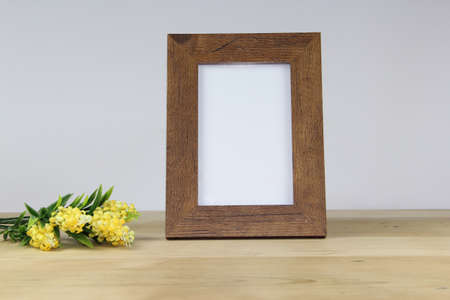Wooden photo frame with yellow flowers on wooden table over white wallの写真素材